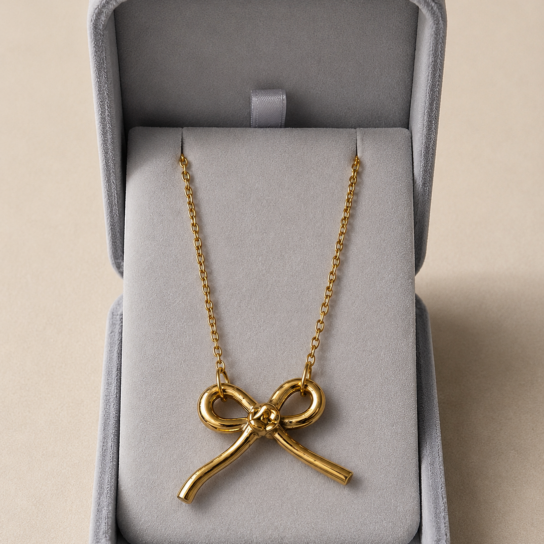 Gold bow-shaped necklace in a gray jewelry box on a beige background
