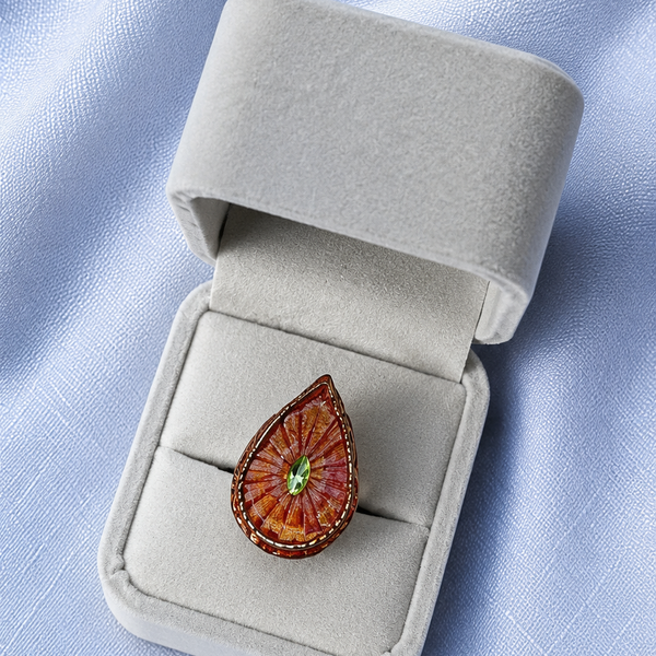 Teardrop-shaped brooch with a green gemstone in a gray jewelry box on a light blue fabric background