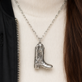 Silver cowboy boot necklace on a person wearing a white sweater and black jacket.